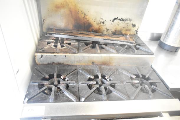 Commercial gas-powered 6 burner range with an oven, 2-tier over shelf, and backsplash, on casters. Signs of use visible.