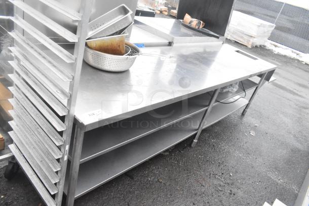 Commercial stainless steel table with two under shelves, features sturdy construction, used condition, visible service label.