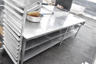 Commercial stainless steel table with two under shelves, features sturdy construction, used condition, visible service label.