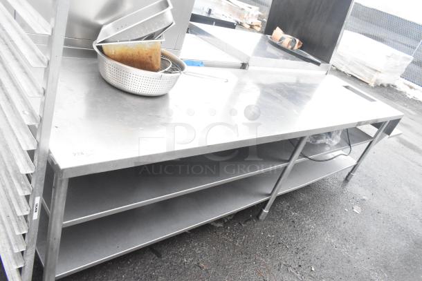 Commercial stainless steel table with 2 undershelves, featuring a flat work surface, adjustable legs, and visible wear.