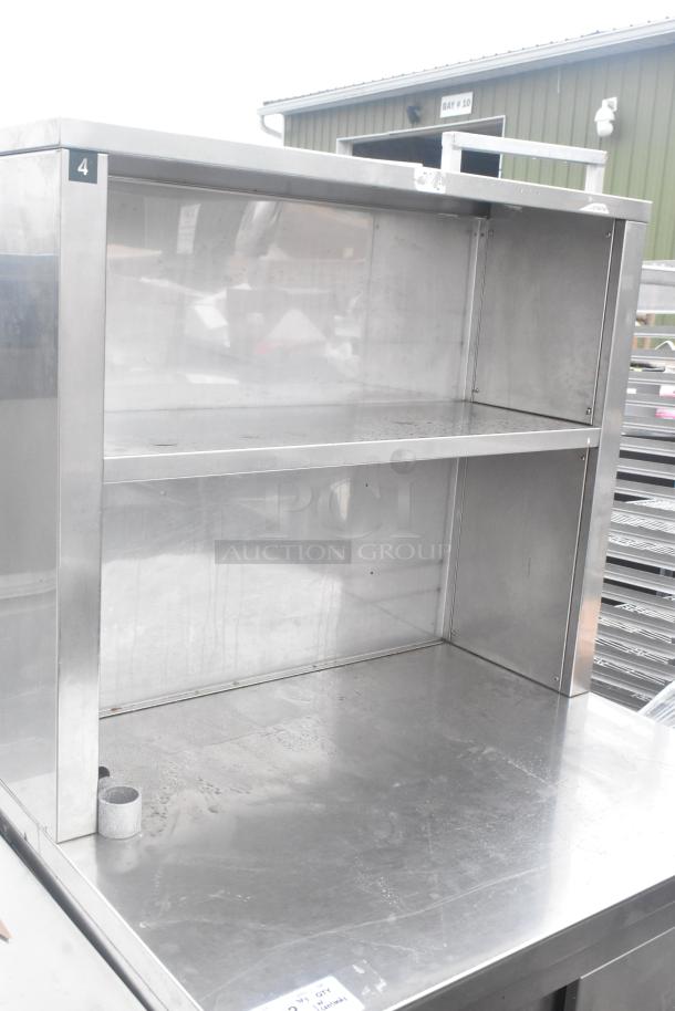 Commercial stainless steel counter with two lower doors, under shelf, over shelf, on casters. Slight wear visible.