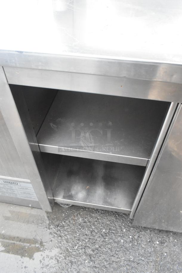 Stainless steel commercial counter with two lower doors, under shelf, over shelf, on commercial casters; good condition.