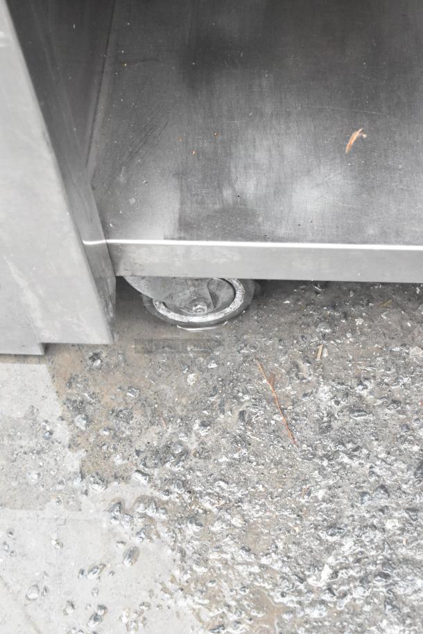 Stainless steel commercial counter with two lower doors, under shelf, over shelf, and sturdy commercial casters.