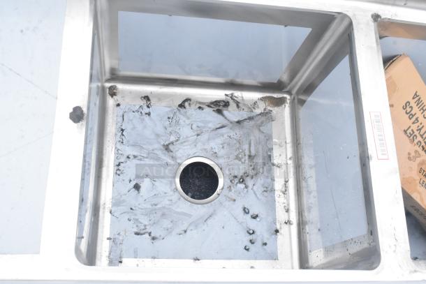 Brand new Regency 600S318181L stainless steel sink with three compartments, stainless legs, left drainboard, and visible debris.