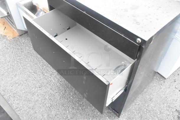 Black 2-drawer filing cabinet with visible scratches and dents; new condition; open drawer with metal interior.