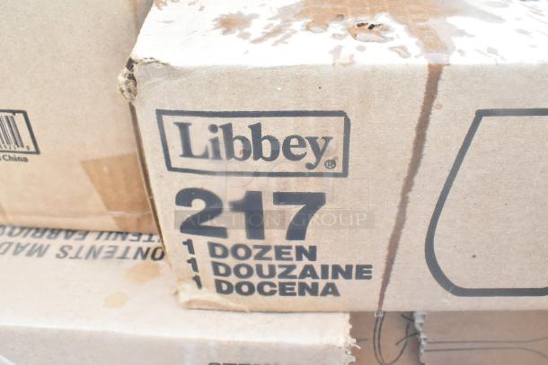 Brown cardboard box with "Libbey 217" printed; indicates one dozen items. Box shows wear. Contains plates, glassware, ramekins.
