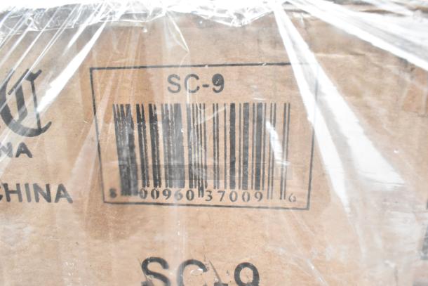 Close-up of a cardboard box labeled "SC-9" with a visible barcode, partially wrapped in plastic.