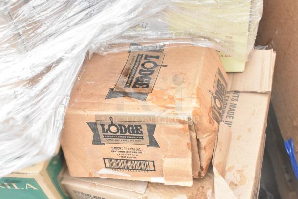 Cardboard box labeled "Lodge" with 5-inch cast iron mini skillets. Box shows slight damage, wrapped in plastic.