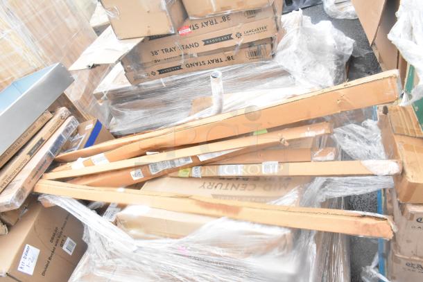 Stack of new scratch and dent items in boxes, including wall corner guards, outdoor tables, and shelves. Labels visible.