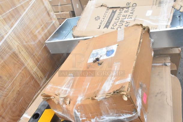 Boxes of scratch and dent items including a Lancaster bar tray stand. Some boxes are damaged or open. Factory labels visible.