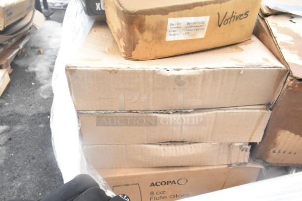 Cardboard boxes containing glassware and dishes, marked with "Acopa 8 oz. Flute Glass" and "Votives." Some boxes show wear.