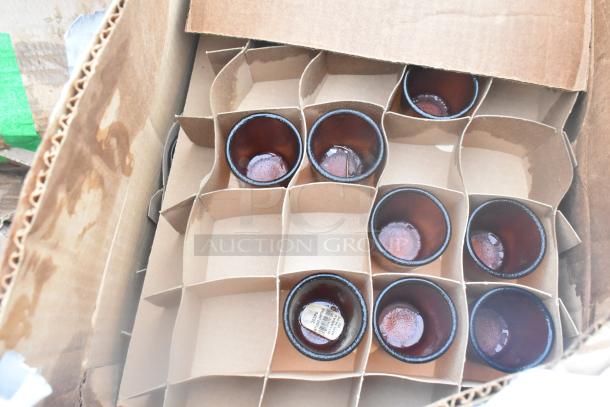 Box of new glassware with brown cups in cardboard dividers. One cup shows a label with item details.