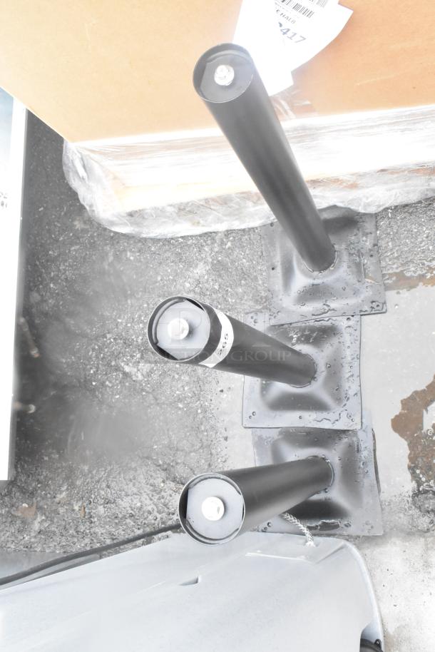 Three black metal table base columns, brand new with minor scratches and dents. Includes protective wrapping. Auction item.