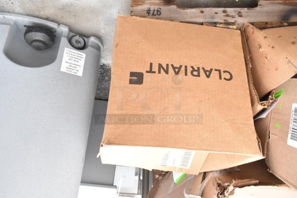 Cardboard box labeled "Clariant" with visible wear next to a large gray container. Box indicates part of a bulk auction lot.