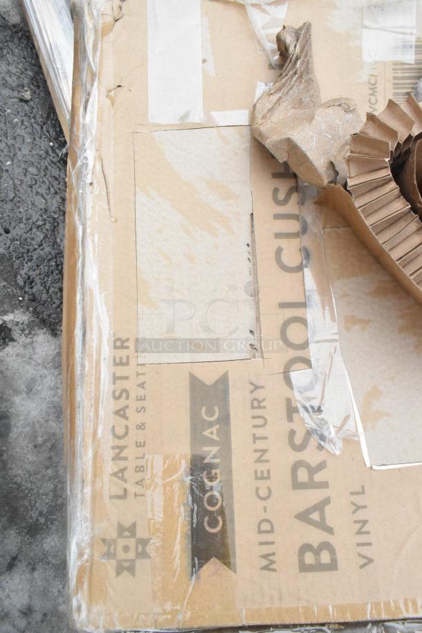 Cardboard box with "Lancaster Table & Seating" and "Mid-Century Bar Stool" text, indicating new furniture item. Packaging shows wear.