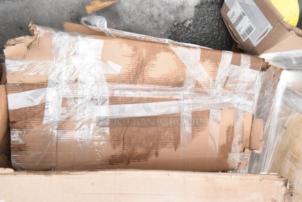 Cardboard packaging with clear plastic wrap, containing scratch and dent items like a floor mat and wall shelf. Labels unclear.