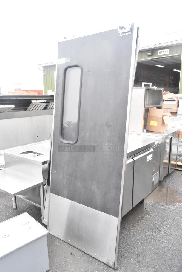 Two swinging kitchen doors with viewing panels and bottom plates, includes hardware, shown outdoors, used condition.