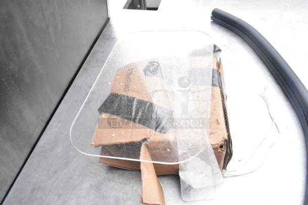 Cardboard box with transparent plastic panel and black tape on metal countertop.