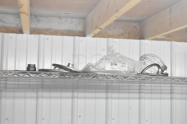 Seven kitchen attachments including a whisk, paddle, dough hook, food processor blades, and grating blade on a shelf.