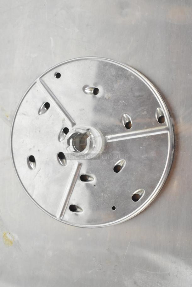 Metal food processor grating blade with perforations and central attachment hub. Appears in used condition.