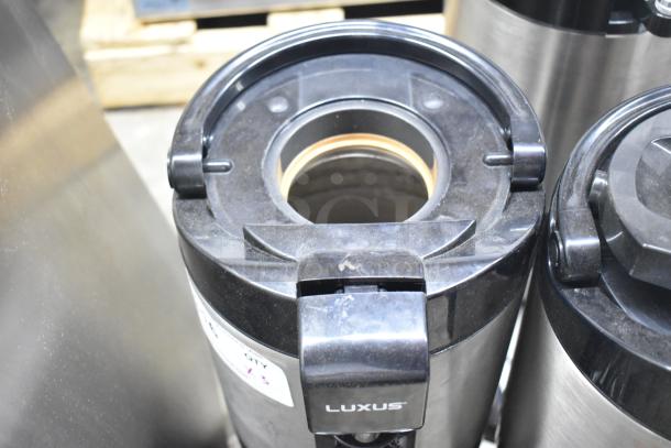 3 Fetco Luxus countertop beverage dispensers, stainless steel, used, with visible Luxus branding on spout.