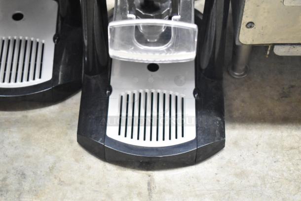 3 Fetco Luxus countertop beverage dispensers, black with slotted drip trays, in used condition, durable design.