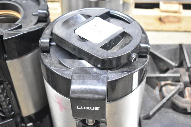 Fetco Luxus countertop beverage dispenser, stainless steel, black lid, visible Luxus branding, used condition.