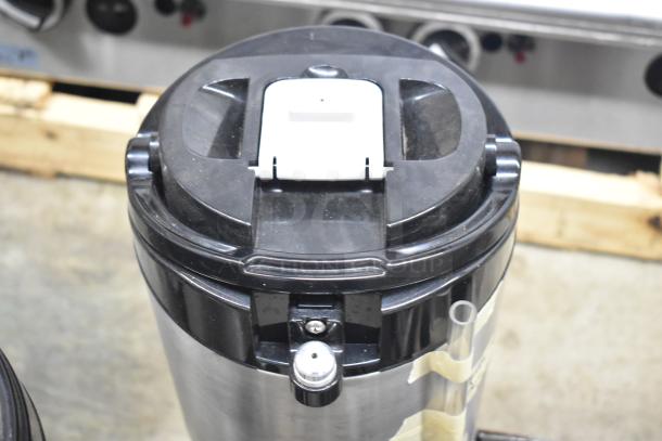 3 Fetco Luxus countertop beverage dispensers, stainless steel, black lids, metal spouts, with visible spout and handle.