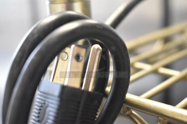 A coiled black power cord with a standard plug is shown partially looped over a metal frame.