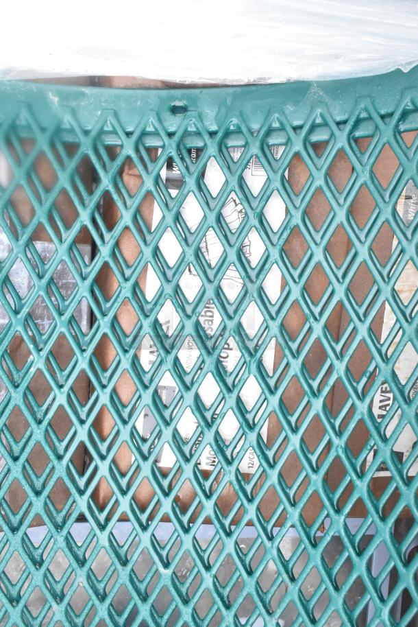 Auction image showing a green diamond-patterned grate partially covering boxes containing brand new scratch and dent items, including mop heads and a trash can shell.