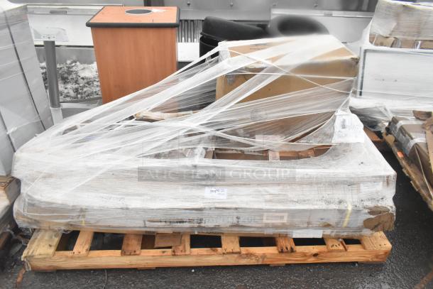 Four brand new scratch and dent items, including a mop sink and work table, wrapped in plastic on a wooden pallet.