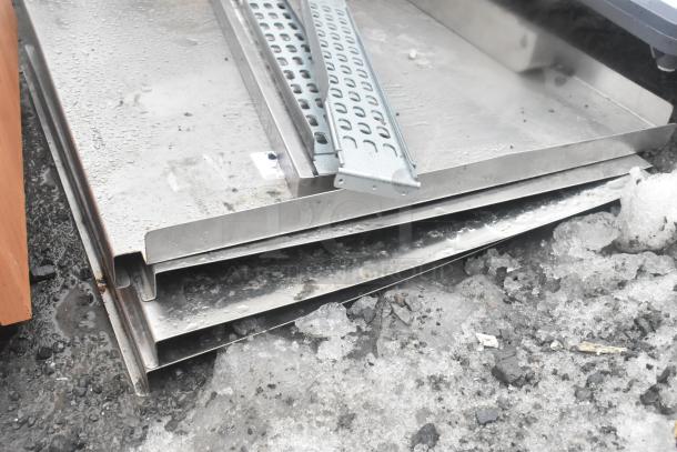 Seven assorted metal sheets and panels, stacked, with visible moisture and snow, showing signs of outdoor exposure.