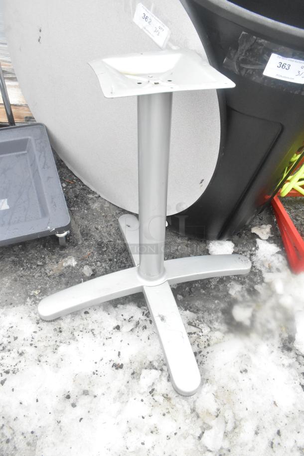 Round gray tabletop with matching gray base, shown in outdoor setting. Visible tag indicates item number. Good condition.