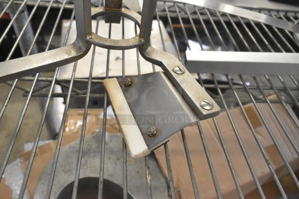 Metal auger on a metal grate, showing rust and wear. Features a sturdy construction with visible bolts and a flat blade.