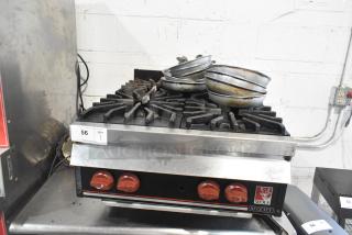 Wolf commercial countertop gas 4-burner range, used condition, red knobs, model label visible, stacked pans on top.