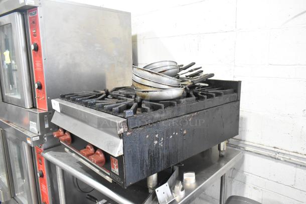 Wolf commercial countertop 4-burner gas range, used. Features red control knobs. Visible wear on surface. Ideal for kitchens.