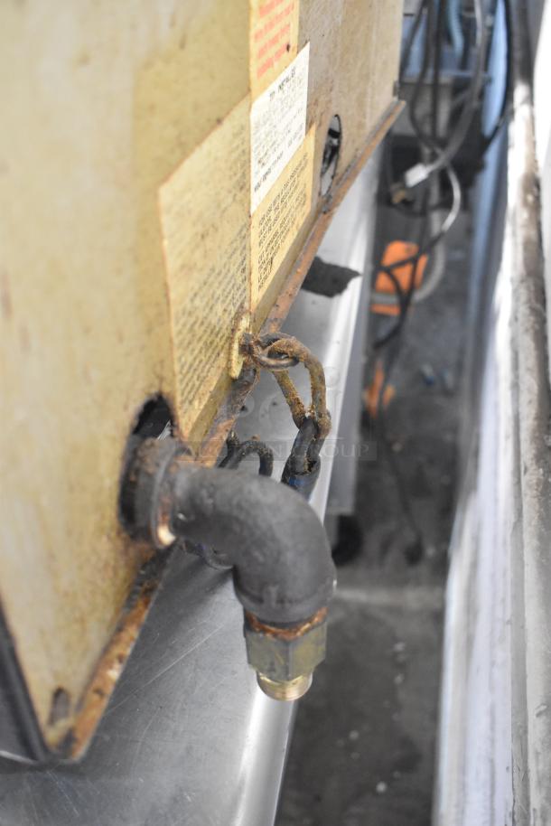 Back view of a Wolf Commercial Countertop Gas Powered 4 Burner Range showing connected gas pipe, labels, and electrical wires.