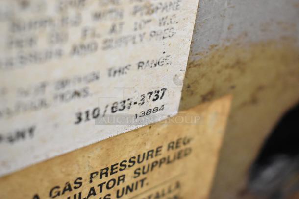 Close-up of worn labels on Wolf Commercial Countertop Gas Powered 4 Burner Range, showing model number and gas pressure info.