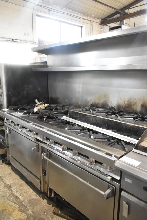Commercial 12 burner gas range with two ovens, overshelf, backsplash, and commercial casters; slight signs of use.