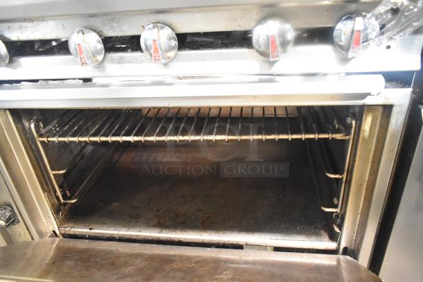 Commercial gas 12-burner range with two ovens, over shelf, backsplash, and casters. Used condition with visible controls.