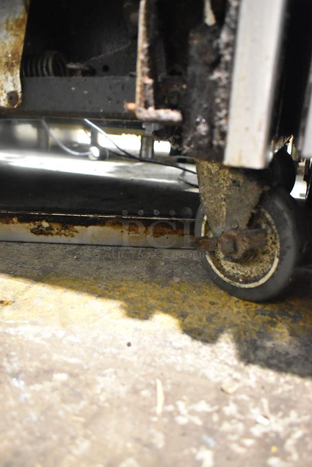 Close-up of commercial range caster, showing rust and wear on wheel and metal components. Part of a 12-burner range unit.