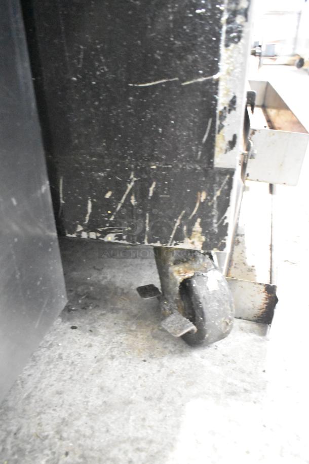 Commercial gas-powered vertical upright broiler on casters, showing wear and scratches. Ideal for kitchen use.