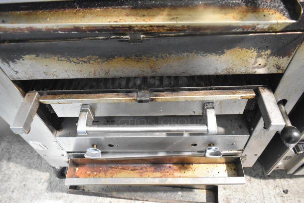 Commercial gas-powered vertical upright broiler, showing signs of use, with handles, control knob, and mounted on casters.