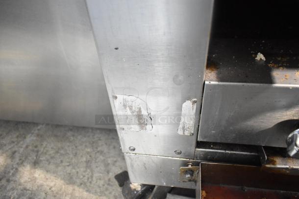 Commercial gas vertical upright broiler on casters, visible wear, industrial metal surface with peeling labels.