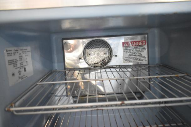 2017 Delfield 406CAP-DD1 undercounter cooler interior, silver fan panel, wire shelves, warning labels visible.