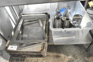 Lot of metal baking pans with rust and plastic bin holding stainless steel pots and dispensers on industrial shelf.