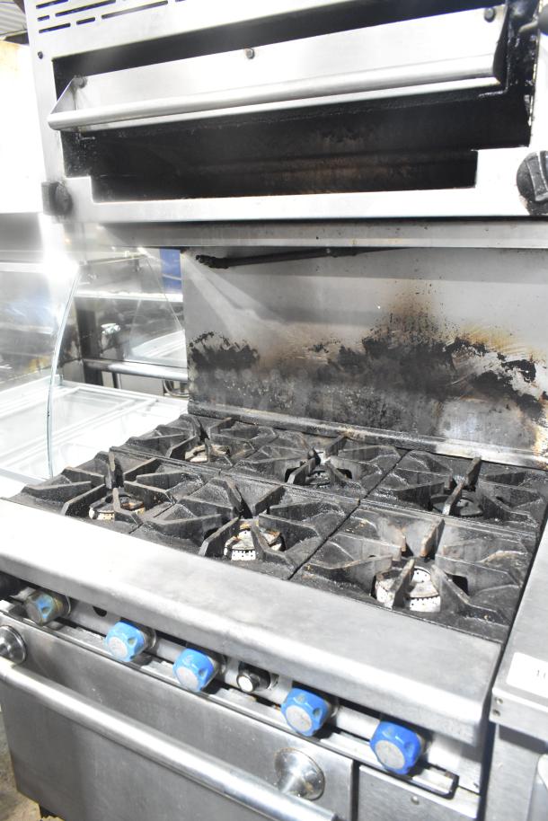 Imperial commercial gas 6-burner range with salamander cheese melter and oven, shows wear, includes blue control knobs.