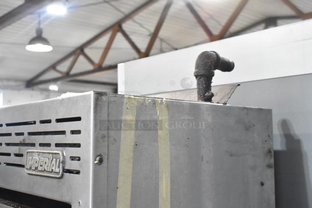 Imperial commercial gas range with 6 burners, salamander cheese melter, and oven. Visible wear, Imperial logo on side.