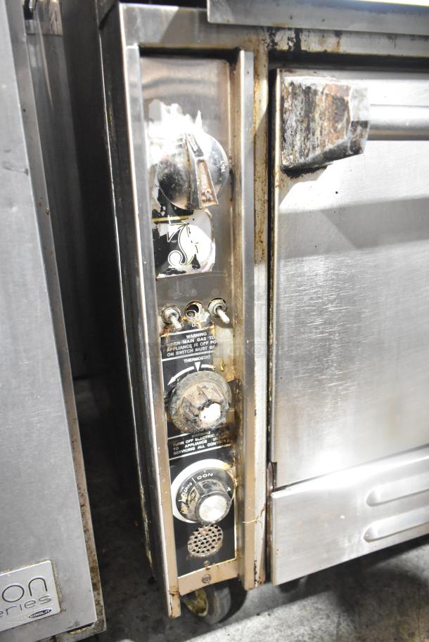 Commercial gas powered 6-burner range with salamander cheese melter and oven. Control knobs and usage markings visible. Signs of wear.