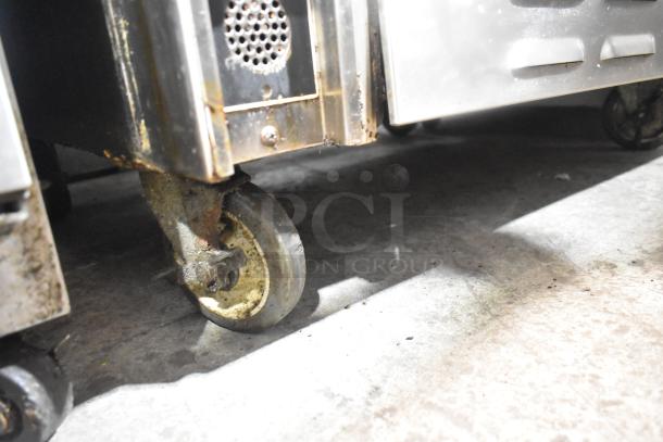 Commercial gas-powered 6 burner range with salamander cheese melter and oven. Visible minor rust on base wheel.